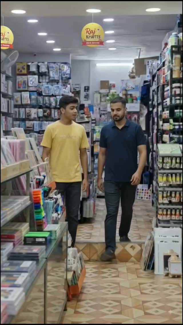 Two shoppers walking down a Raj Krafts aisle lined with notebooks and paints
